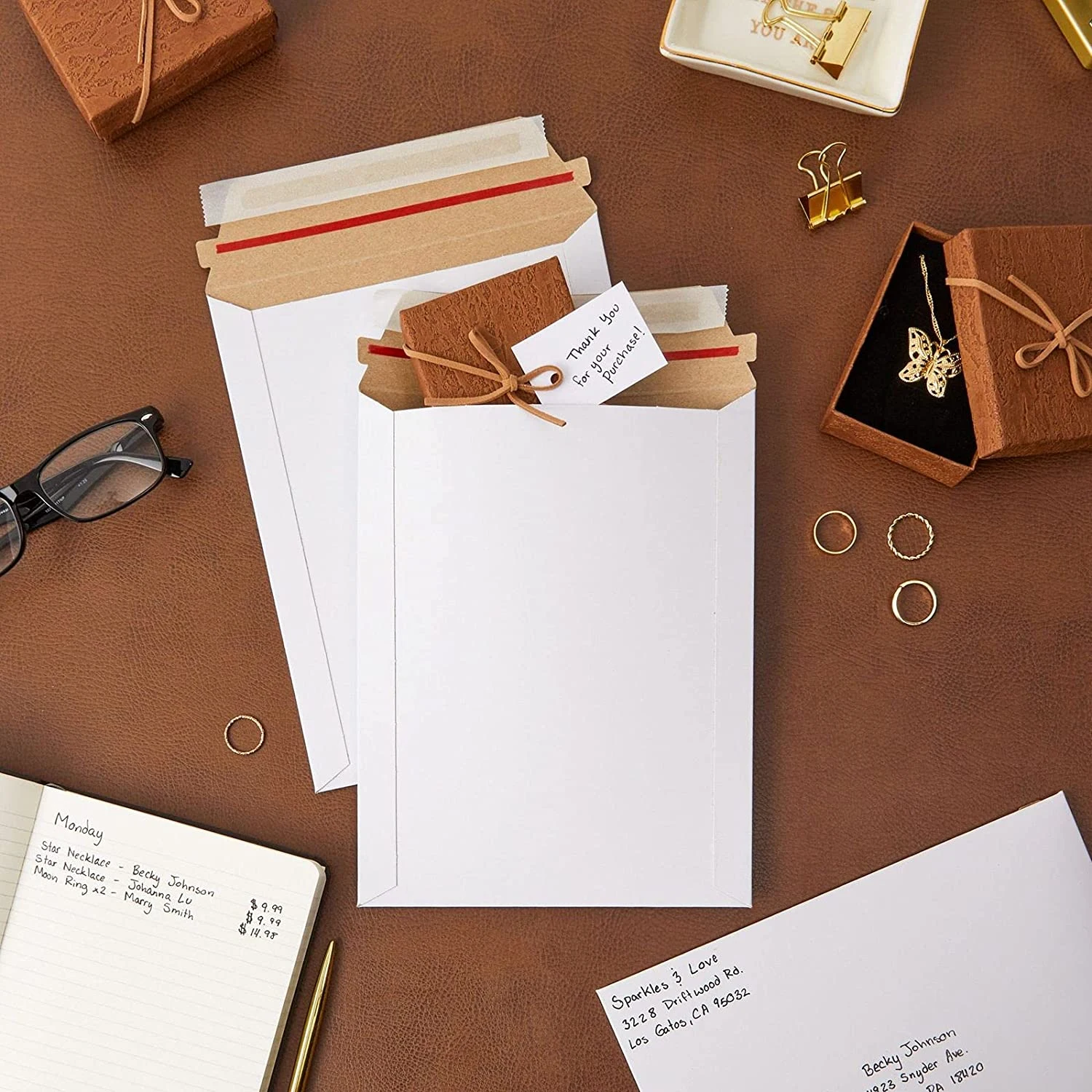 White paper mailers with red release strips on the sealing flaps, on a brown table.